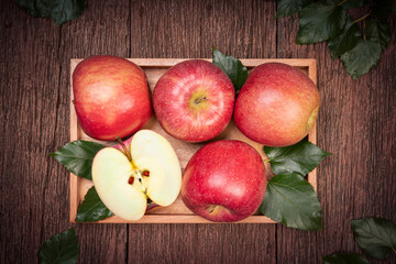 San Fuji Apples in wooden basket on wooden table in garden, Pink Apple with leaves in wooden background.