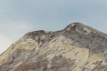 A stockpile of salt or sodium chloride road salt, halite, rocksalt stockpiled for winter snow and ice deicing controls. The road salt is piled in one mound with the top portion against a blue sky.