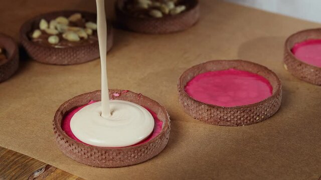 Chef adding white cream to the small tarts with chokolate