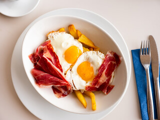 Plate of appetizing hearty breakfast of fried eggs with slices of delicious bacon and French fries
