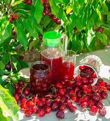 Closeup of fresh ripe red sweet cherries, mason jar of compote with berries and carafe with cherry...