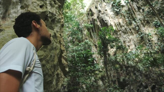 Close up of a young man face outside a cave in a tropical jungle looking around in slowmotion.
