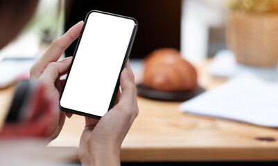 Mockup image blank white screen cell phone.women hand holding texting using mobile on desk at home office.