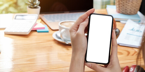 Mockup image blank white screen cell phone.women hand holding texting using mobile on desk at home office.