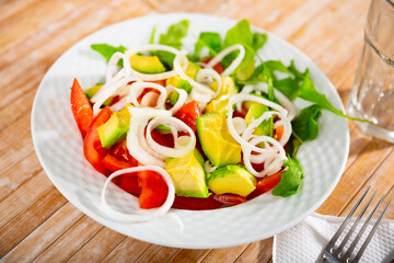 Organic mediterranean arugula salad with avocado and tomato on a plate in cafe