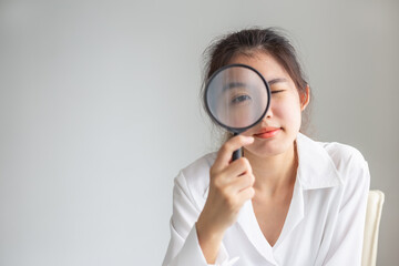 Asian woman looking through magnifying glass, searching or investigating something.
