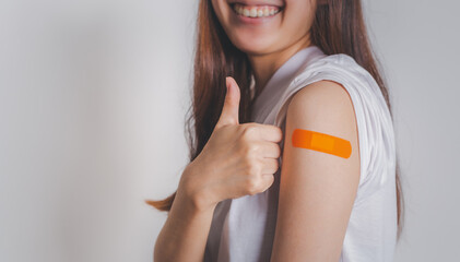 Asian woman showing thumb up gesture and shows off an orange bandage after receiving the covid-19...