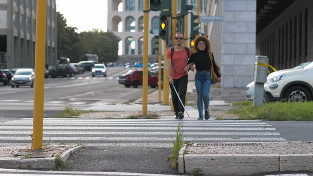  young smiling woman helps his blind friend to cross the street