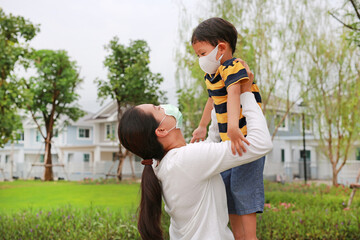 Asian mom carrying her son with wearing protective face mask both in public garden during coronavirus and flu outbreak
