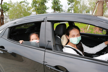 Asian mom and daughter wears hygiene face mask lying in car with looking through camera during coronavirus (covid-19) outbreak
