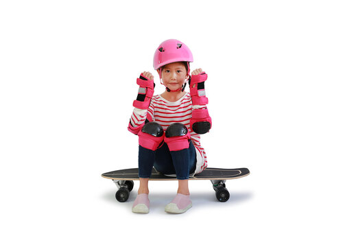 Young Asian girl skateboarder with safety and protective equipment raise hands up for strong gesture sit on skateboard isolated on white background. Image with Clipping path