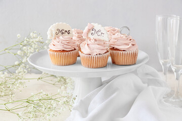 Dessert stand with tasty cupcakes and wedding rings on table