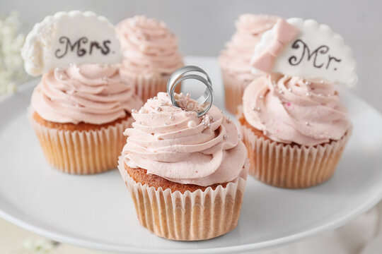 Dessert stand with tasty cupcakes and wedding rings, closeup