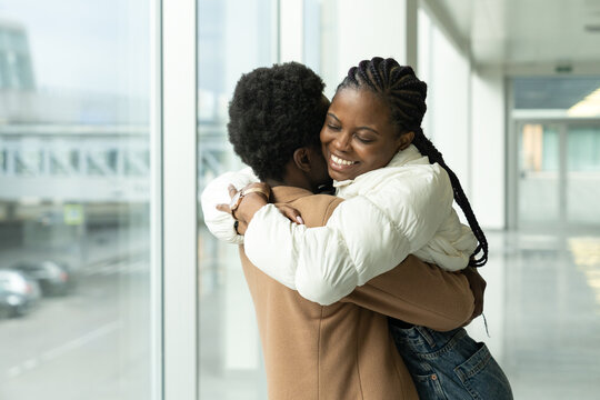 Couple reunion in airport: portrait of happy african american female met hug boyfriend arriving from vacation trip abroad. Lovers after long separation due to coronavirus epidemic meet at end of covid