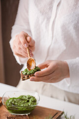 Woman making tasty toast with pesto sauce, closeup