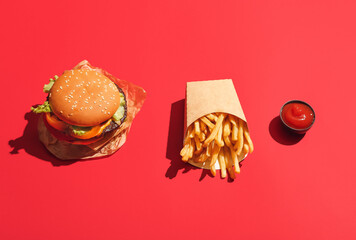 Paper box with tasty french fries, tomato sauce and burger on color background