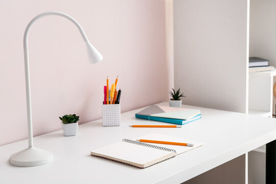 Modern lamp with stationery on table near color wall