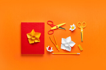 Origami daffodils and stationery on color background