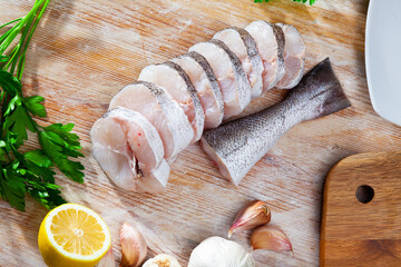 Raw steaks of hake with lemon and greens ready for cooking on the wooden surface