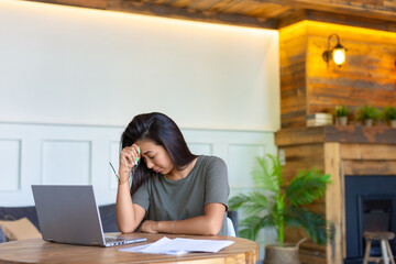 Photo of an exhausted asian woman working at home before the deadline. Conceot of modern technologies in everyday life.