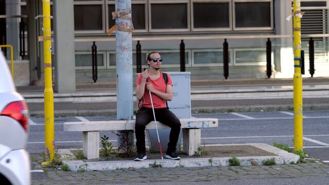 handicap, disability - blind man sitting on a bench waiting to cross the road