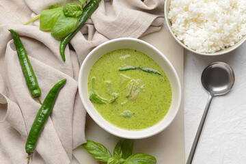 Bowl of tasty green chicken curry and ingredients on light background