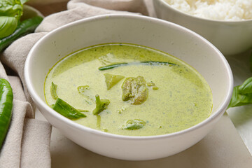 Bowl of tasty green chicken curry on light background, closeup