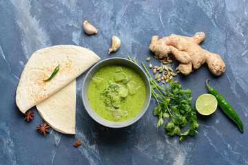 Bowl of tasty green chicken curry and ingredients on color background