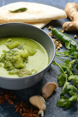 Bowl of tasty green chicken curry and ingredients on color background, closeup