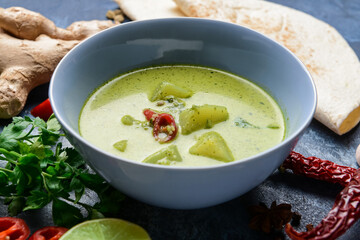Bowl of tasty green chicken curry and ingredients on color background, closeup
