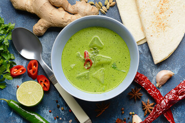 Bowl of tasty green chicken curry and ingredients on color background