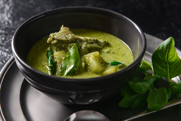 Bowl of tasty green chicken curry on dark background, closeup