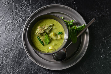 Bowl of tasty green chicken curry on dark background
