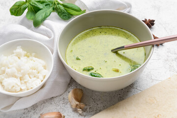 Bowl of tasty green chicken curry and ingredients on light background