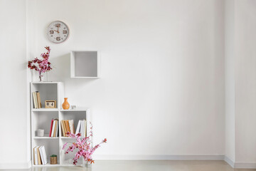 Book shelf with blossoming branches near light wall