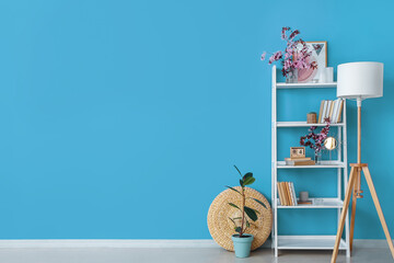 Book shelf with blossoming branches and lamp near color wall