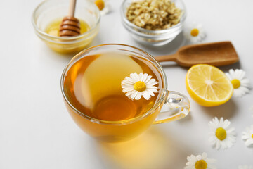 Composition with tasty chamomile tea, flowers and honey on grey background