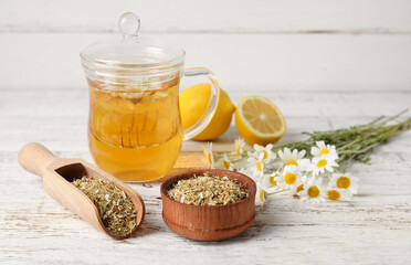 Composition with tasty chamomile tea, flowers and lemon on light wooden background