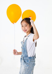 Portrait close up isolated studio shot of young pretty cute long black hair preschooler girl in jeans denim skirt overalls standing smiling look at camera holding two orange balloon sticks in hands