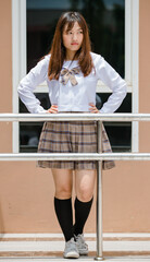 Full length portrait of young attractive female asian high school students in white shirt brown checkered school uniform arm cross in school campus smiling