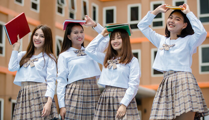 Group of four young attractive asian female high school students in brown checkered school uniform standing together in school campus smiling. Concept for education high school students life