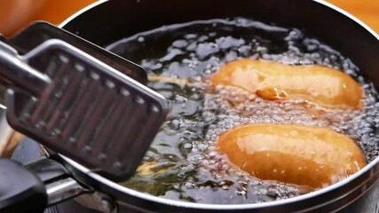 Sausage skewers coated in batter and fried in hot oil in a pan on the kitchen stove. Homemade corndog. cooking process.