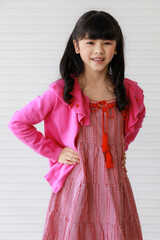 Little adorable sweet cheerful Asian girl wearing pink clothes, pretty joyful smiling with happiness, posing, standing and looking at camera.