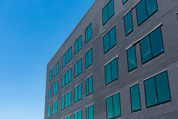 Exterior view of commercial building under construction. The wall is covered with black insulation material. Blue sky.