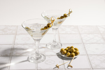 Martini cocktail with olives on the tiled table. An alcoholic classic drink with ice in an elegant glass