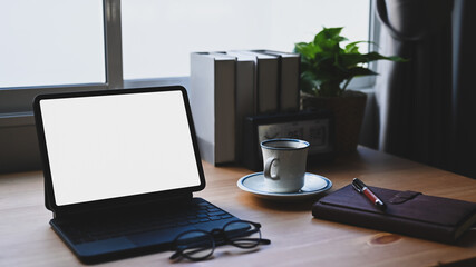 Comfortable workspace with computer tablet, books and coffee cup on wooden desk.