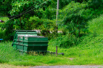 A large green bin is a collection point for local villagers to place waste in the green grass area.