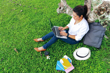 Girl enjoy listening music and reading a book and play laptop on the grass field of the park in the morning. Lifestyle Concept.