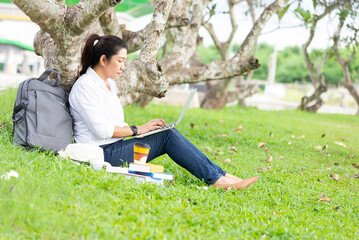 Girl enjoy listening music and reading a book and play laptop on the grass field of the park in the morning. Lifestyle Concept.