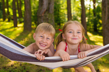 Happy little kids brother and sister lie in a hammock and wipe off video on the phone